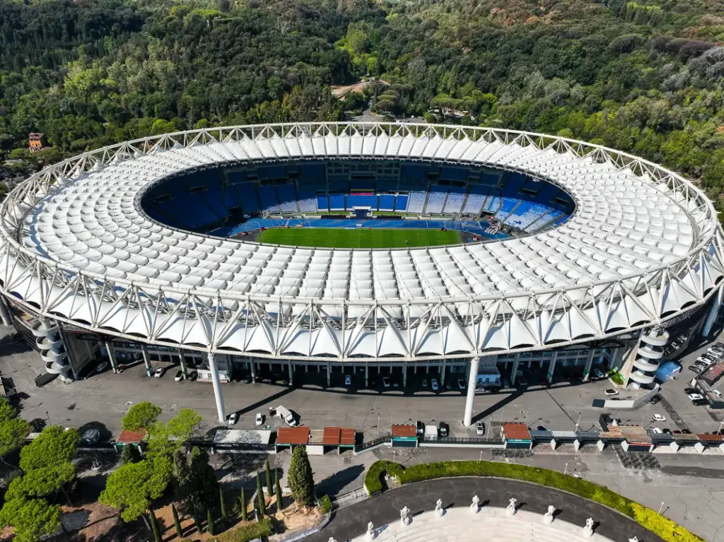 Sfotografowany z drona w samo południe Stadio Olimpico, z silnym kontrastem między białym zadaszeniem a głębokim cieniem rzucanym na trybuny