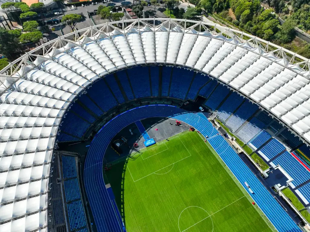Detale architektoniczne jasnego zadaszenia Stadio Olimpico oświetlone mocnym, południowym słońcem z perspektywy drona.