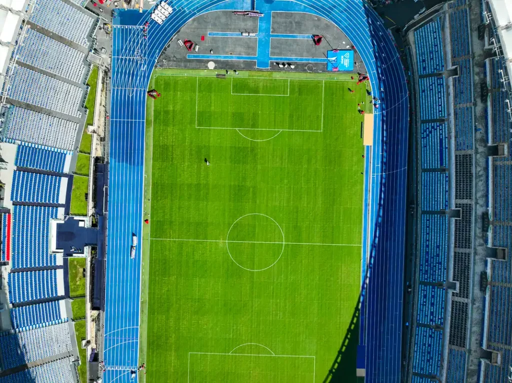 Jasna korona Stadio Olimpico wyraźnie odcinająca się od otaczających go zielonych drzew w mocnym, rzymskim słońcu